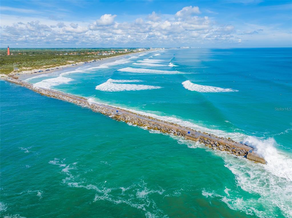 An aerial view of a stone jetty extending into the ocean near a sandy beach — 4873 S ATLANTIC AVENUE, PONCE INLET, FL