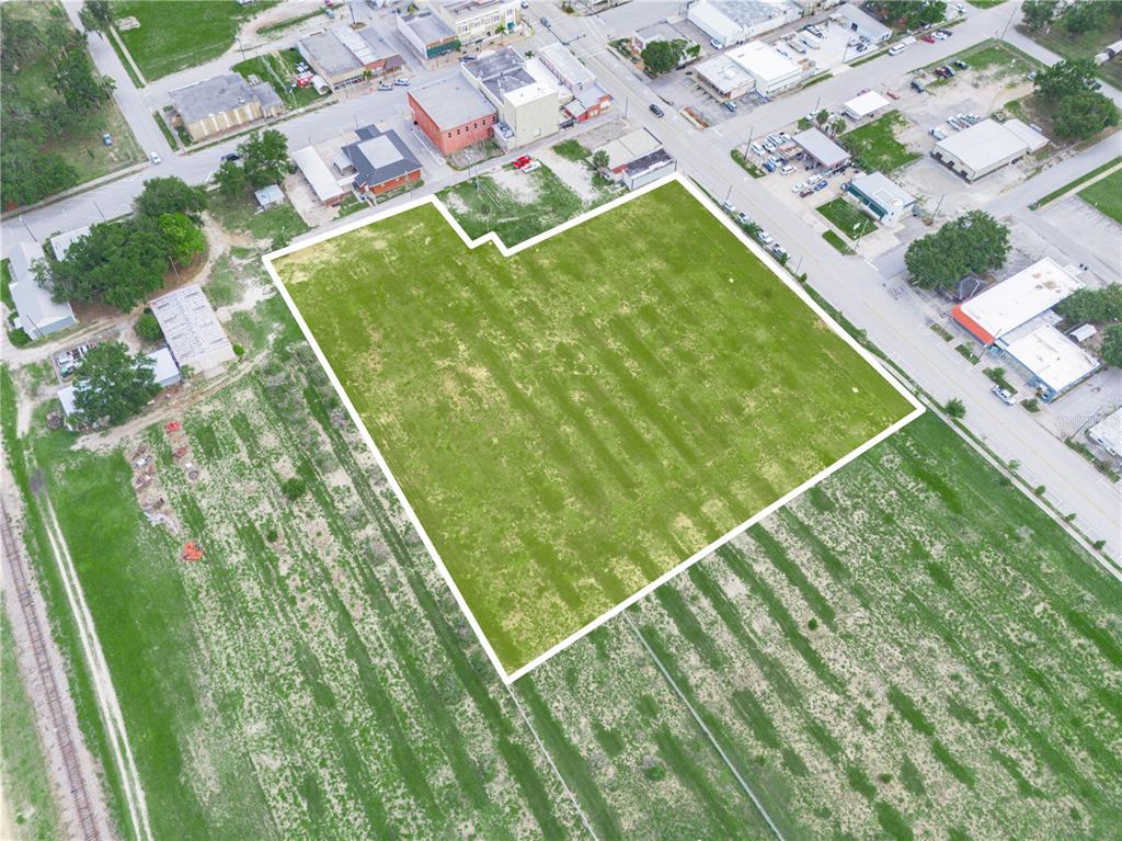 An aerial view shows a large, vacant, grass-covered lot outlined in white within a town — N SCENIC HIGHWAY, FROSTPROOF, FL