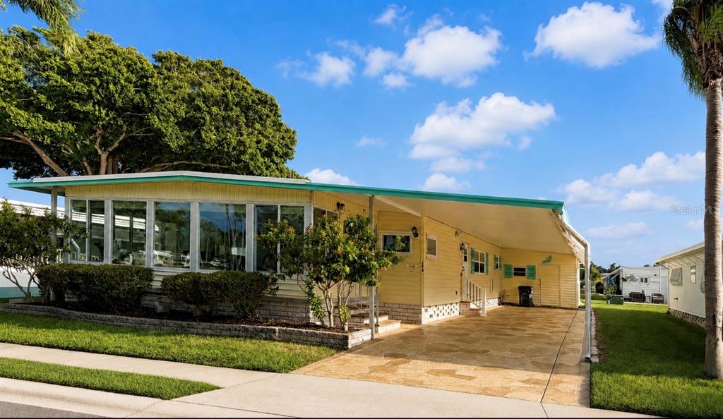 A yellow mobile home features a large glass-enclosed sunroom and a stone-paved carport — 1100 BELCHER ROAD S UNIT 304, LARGO, FL