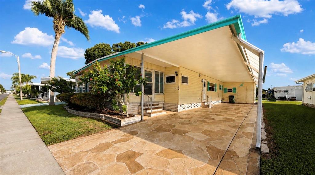 A yellow mobile home features a large carport with a stone-patterned concrete driveway — 1100 BELCHER ROAD S UNIT 304, LARGO, FL