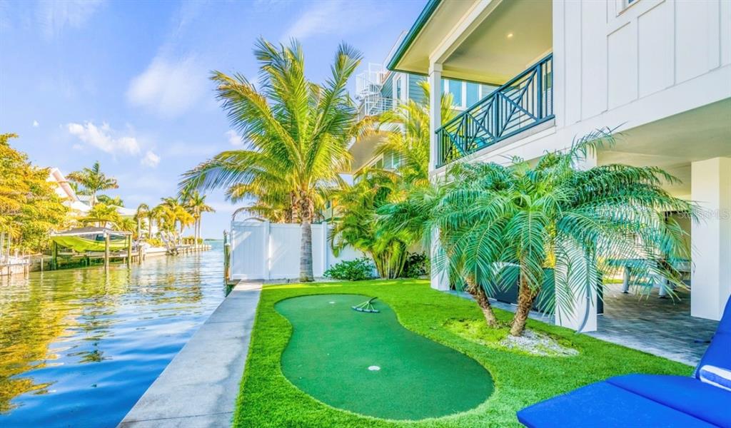 A waterfront home features a backyard putting green, palm trees, and a covered patio area — 401 20TH PLACE, BRADENTON BEACH, FL