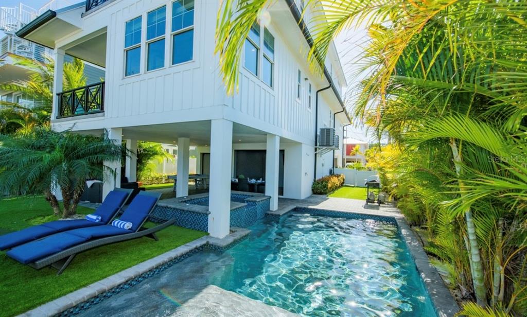 A white house on stilts features a swimming pool, hot tub, and lounge chairs — 401 20TH PLACE, BRADENTON BEACH, FL