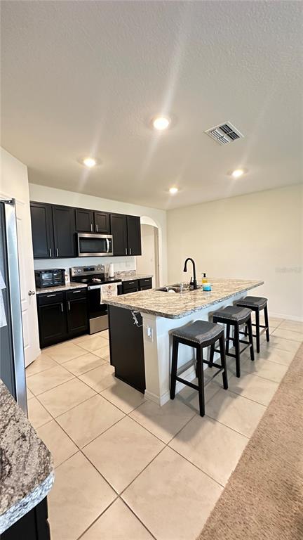A kitchen features dark cabinets, granite countertops, a center island with bar stools, and stainless appliances — 476 BOARDWALK AVENUE, HAINES CITY, FL