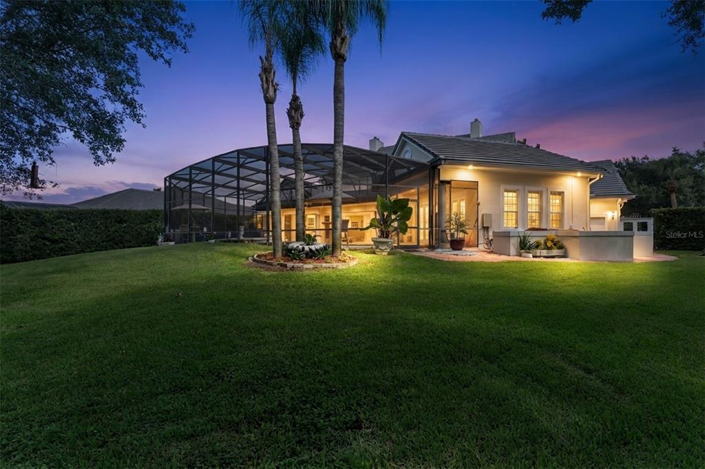 A backyard view of a house with a screened-in pool enclosure and palm trees — 1516 SUNSET POINTE PLACE, KISSIMMEE, FL