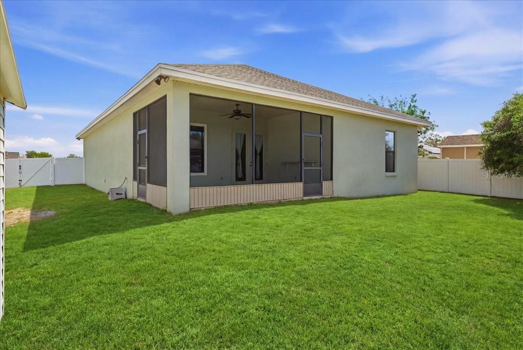 A backyard view of a house with a screened-in porch and a white vinyl fence — 1789 KINGSMILL DRIVE, BARTOW, FL