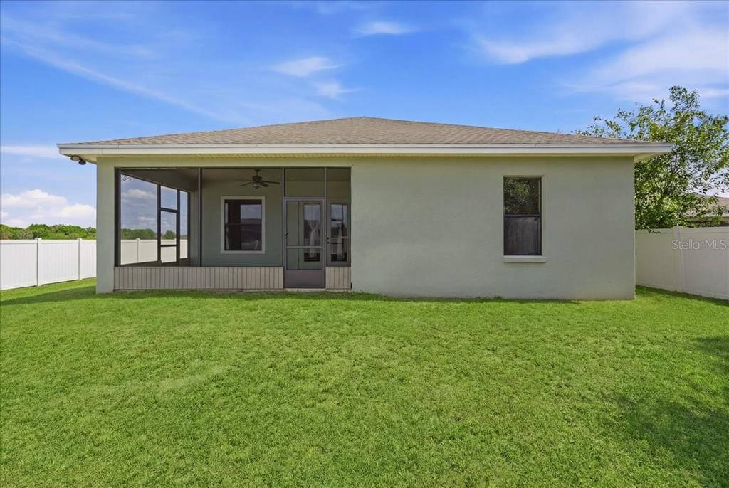 The exterior rear view of a house features a screened-in porch and a grassy yard — 1789 KINGSMILL DRIVE, BARTOW, FL
