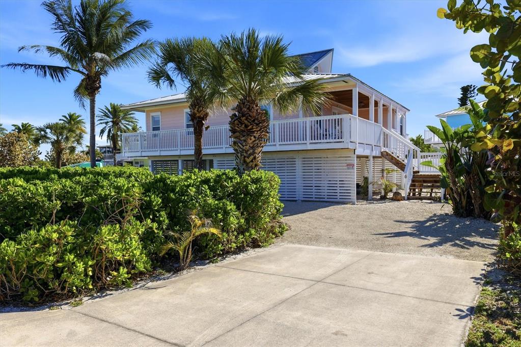 A light pink elevated house with a white wraparound porch stands behind a gravel driveway — 11 BOCILLA DRIVE, PLACIDA, FL