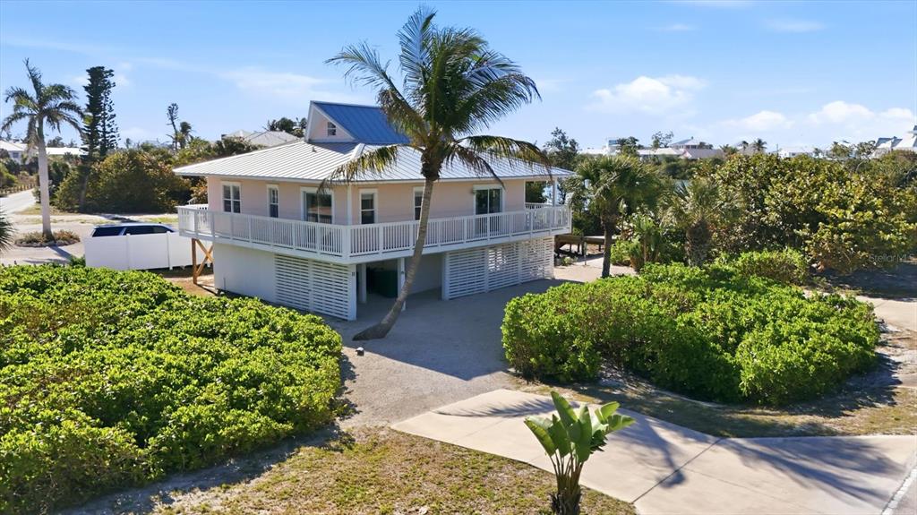 An elevated, light-colored house with a metal roof sits on a gravel lot with landscaping — 11 BOCILLA DRIVE, PLACIDA, FL