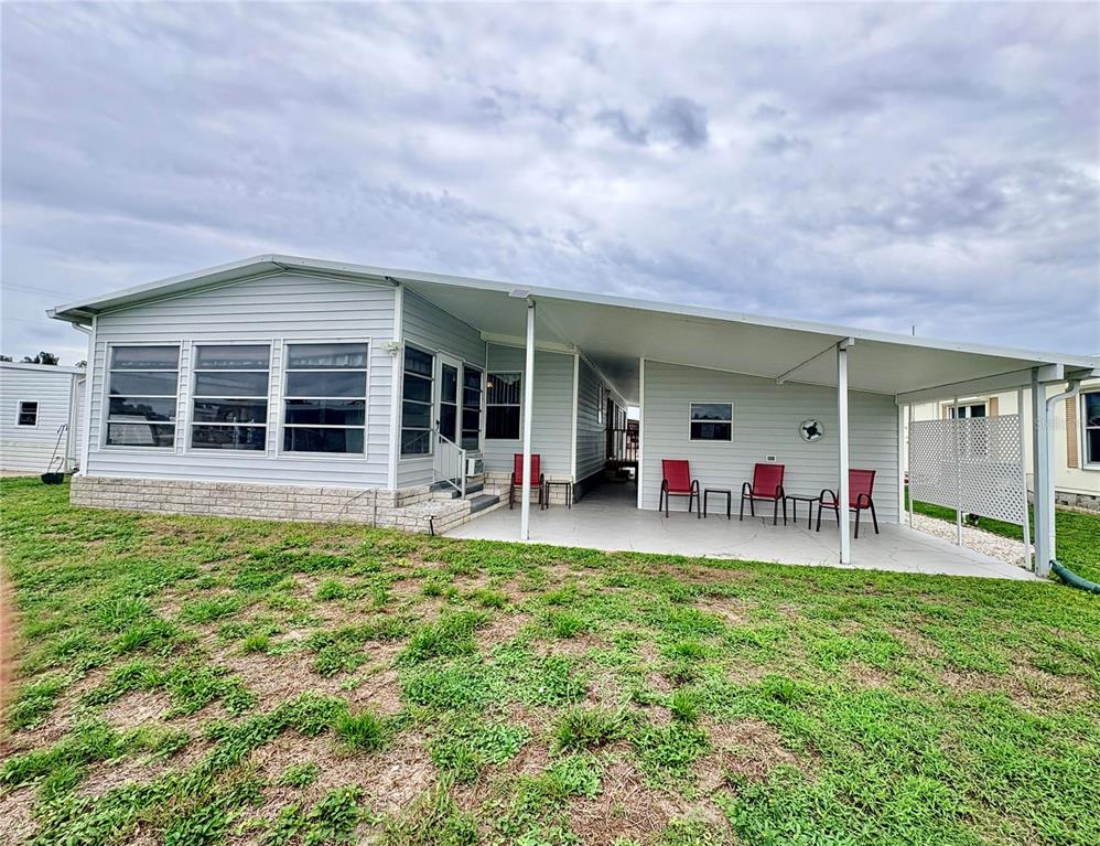 The exterior of a light-gray manufactured home features a large covered patio and lawn — 3163 INDIAN VILLAGE LANE, NORTH FORT MYERS, FL