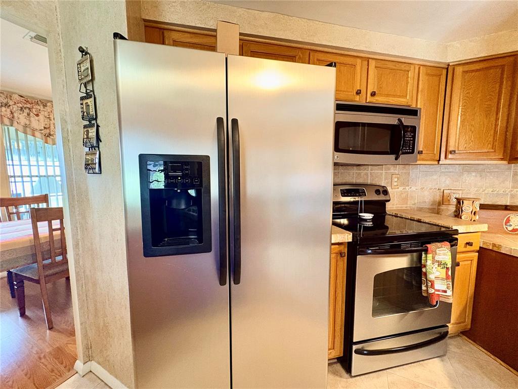 A kitchen features stainless steel appliances, wood cabinets, and a view into the dining area — 3163 INDIAN VILLAGE LANE, NORTH FORT MYERS, FL