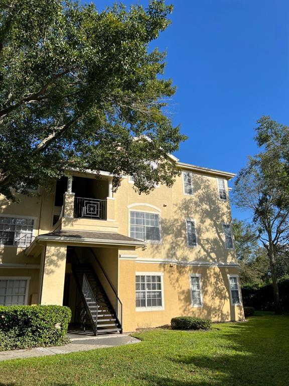 A three-story yellow apartment building features an exterior staircase and a balcony with metal railings — 2674 ROBERT TRENT JONES DRIVE UNIT 334, ORLANDO, FL