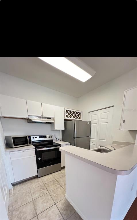 A kitchen features white cabinets, stainless steel appliances, a tiled floor, and a breakfast bar — 2674 ROBERT TRENT JONES DRIVE UNIT 334, ORLANDO, FL