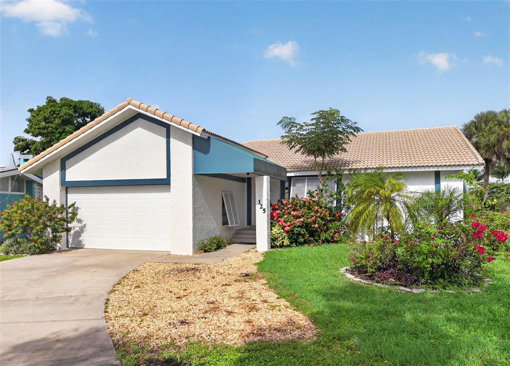 A single-story house with a white stucco facade, blue trim, and a gravel driveway — 125 DONNA COURT, PUNTA GORDA, FL