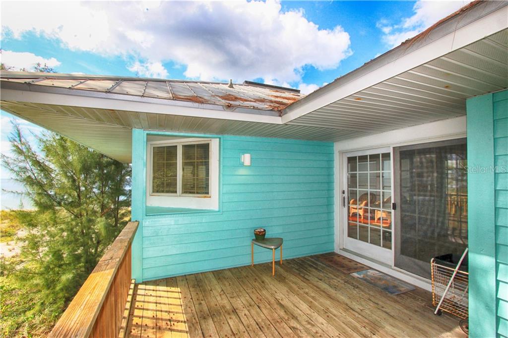 A wooden deck with a small stool and sliding glass doors against a turquoise exterior wall — 181 N GULF BOULEVARD UNIT 4, PLACIDA, FL