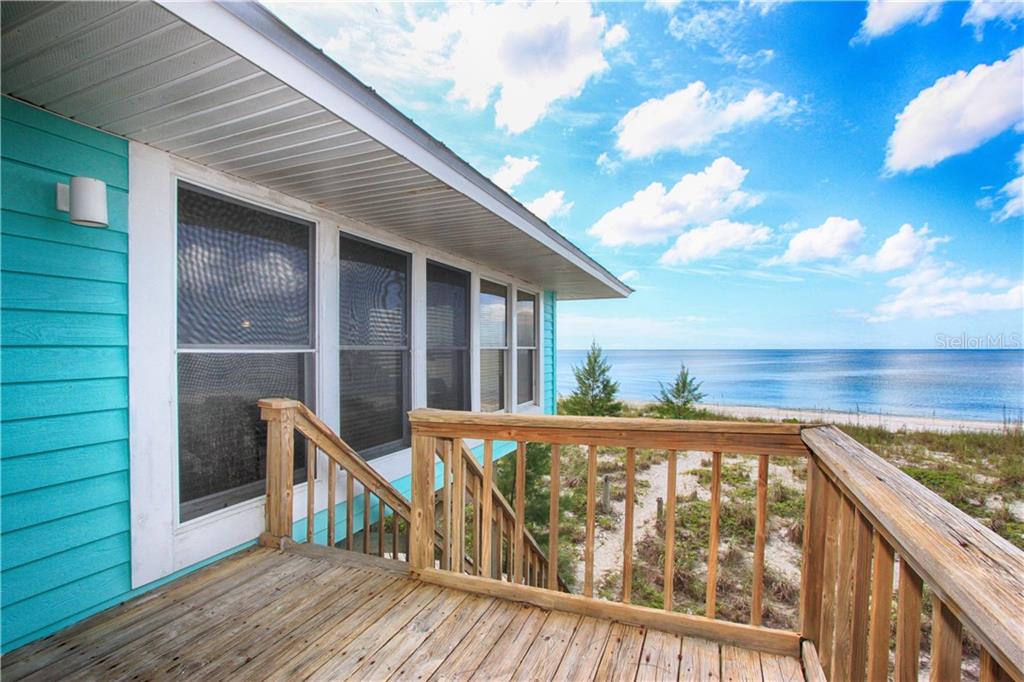 A wooden deck with railings overlooks a sandy beach and the ocean under a blue sky — 181 N GULF BOULEVARD UNIT 4, PLACIDA, FL