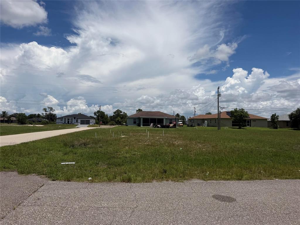 A vacant grassy lot sits in front of several suburban houses under a cloudy sky — 2829 NE 5TH AVENUE, CAPE CORAL, FL