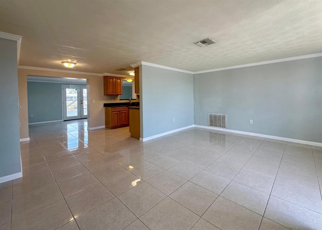 An open-concept living area features light-colored tile flooring and a view into the kitchen — 12812 4TH ISLE, HUDSON, FL