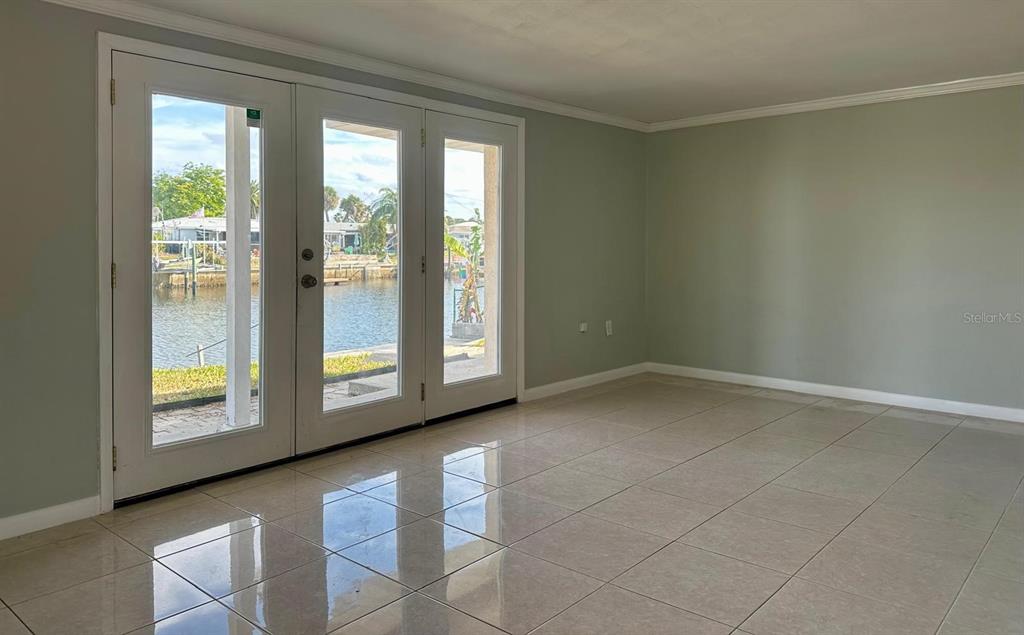 A room with light-colored tile flooring and glass doors opening to a waterfront view — 12812 4TH ISLE, HUDSON, FL