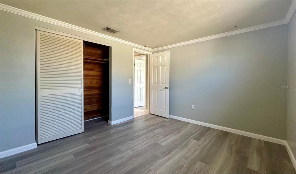 A bedroom features gray walls, wood-look flooring, a sliding louvered closet door, and an open doorway — 12812 4TH ISLE, HUDSON, FL