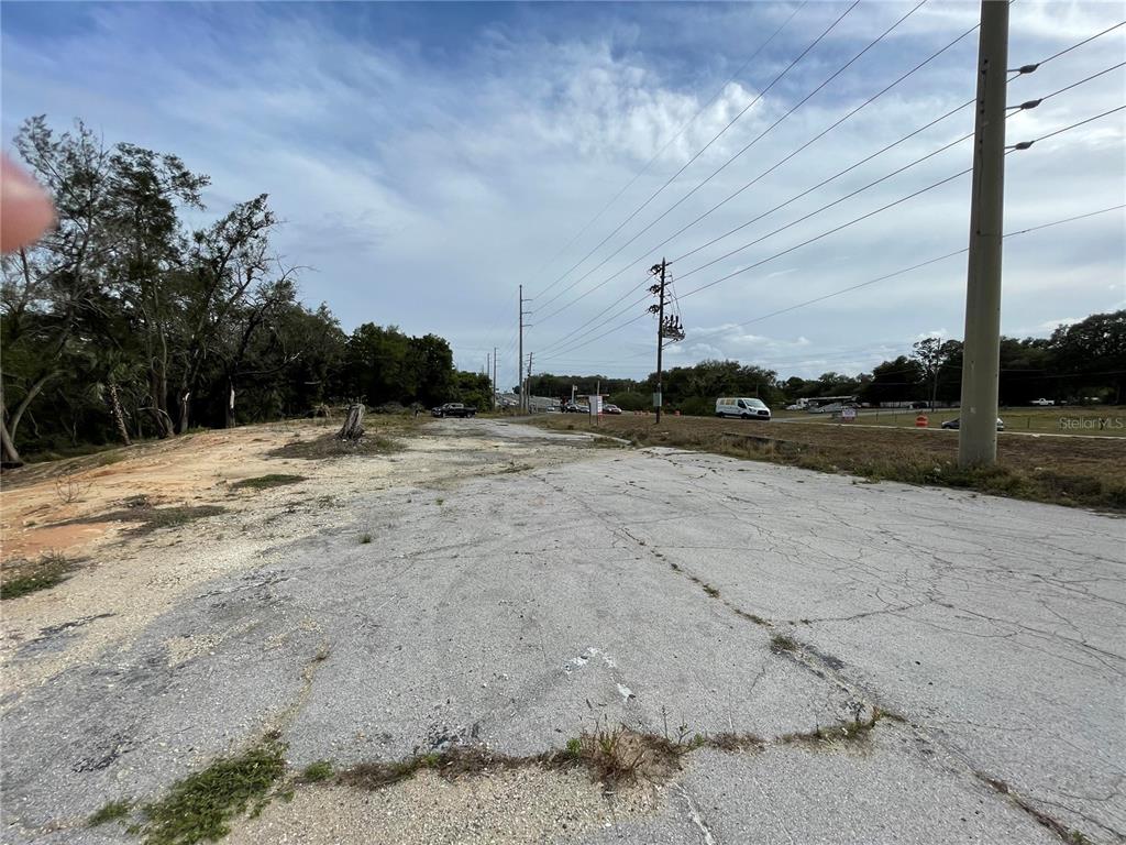 An empty, cracked asphalt lot sits beside a grassy area with utility poles and trees — 2011 US HIGHWAY 441/27, FRUITLAND PARK, FL