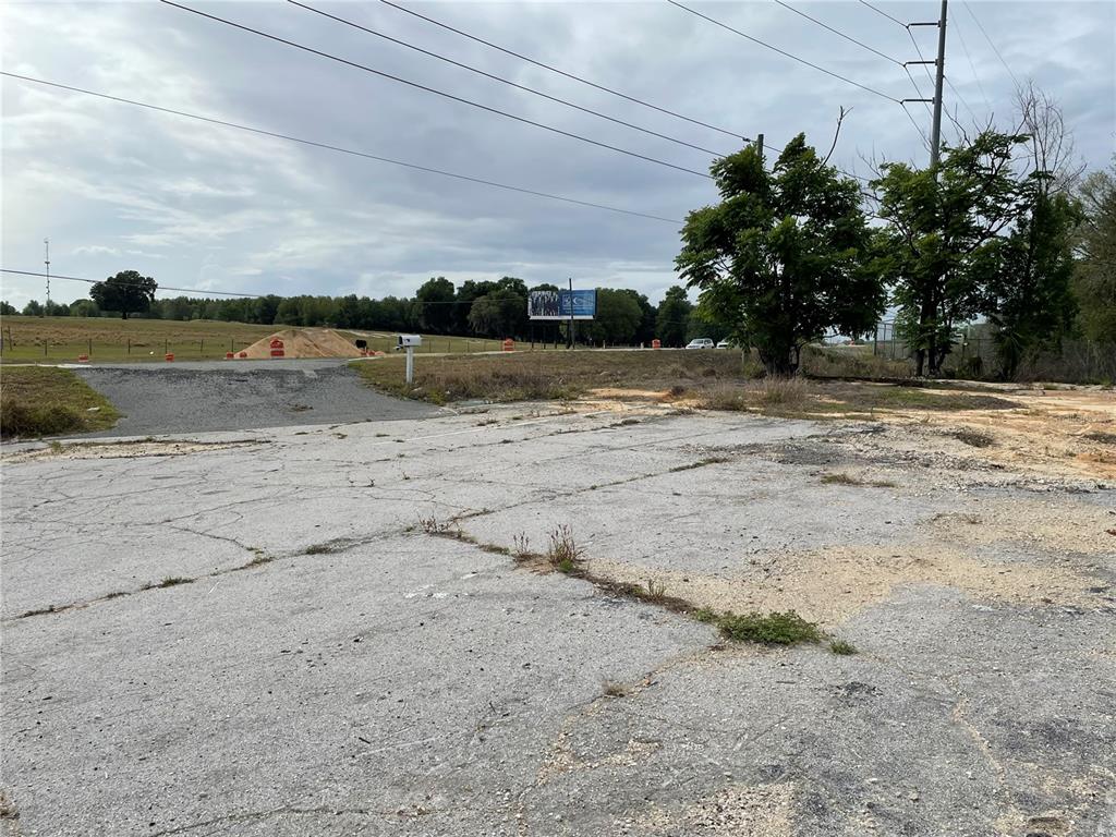 A cracked asphalt lot sits before a grassy field with a billboard and power lines — 2011 US HIGHWAY 441/27, FRUITLAND PARK, FL