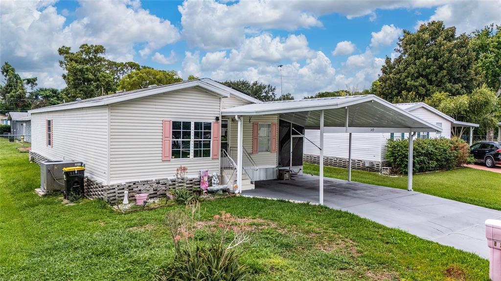 A single-story manufactured home with light siding, pink shutters, and an attached metal carport — 149 JANA CIRCLE, AUBURNDALE, FL