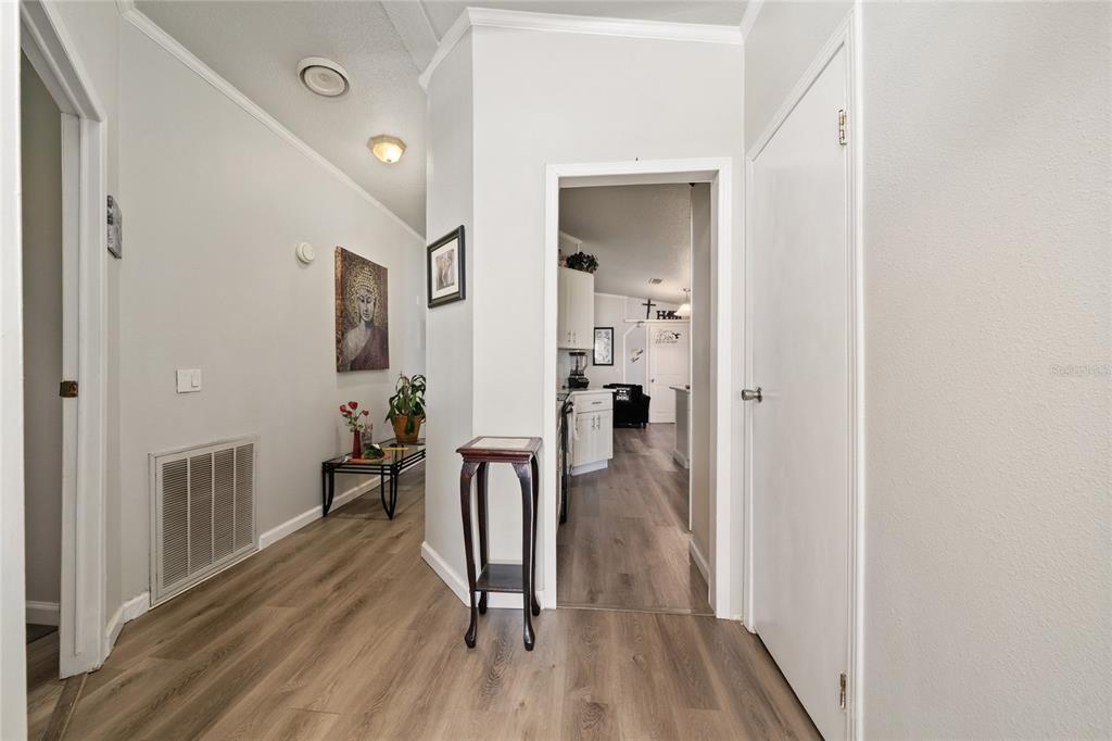 A hallway with wood-look flooring leads into a kitchen area with white cabinets — 149 JANA CIRCLE, AUBURNDALE, FL