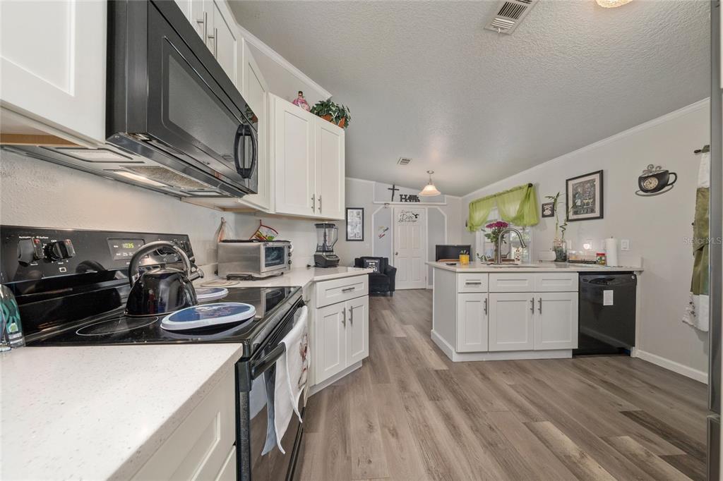 A kitchen features white cabinets, black appliances, a central island, and wood-look flooring — 149 JANA CIRCLE, AUBURNDALE, FL