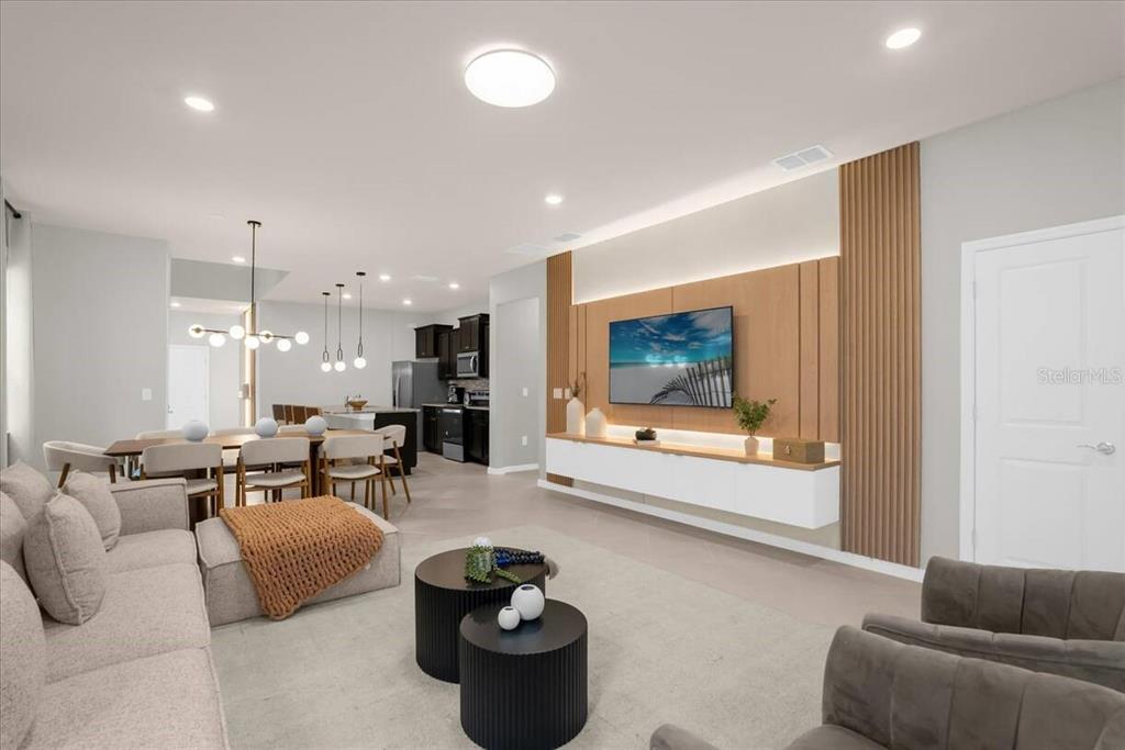 A modern open-concept living room features a wood-paneled media wall, white cabinetry, and dining area — 16225 SAINT KITTS CIRCLE, CLERMONT, FL