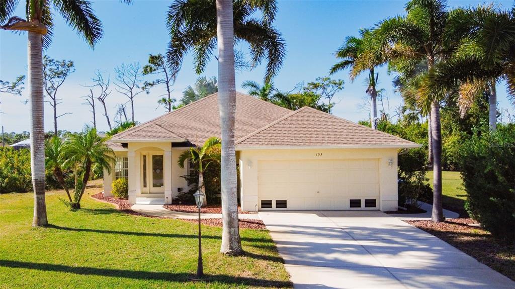A single-story house with a beige stucco exterior, a two-car garage, and several palm trees — 101 & 103 WAHOO DRIVE, ROTONDA WEST, FL