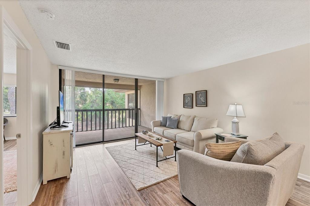 A living room features light wood flooring, a beige sofa, and a sliding glass balcony door — 5264 LAKE VILLAGE DRIVE UNIT 48, SARASOTA, FL