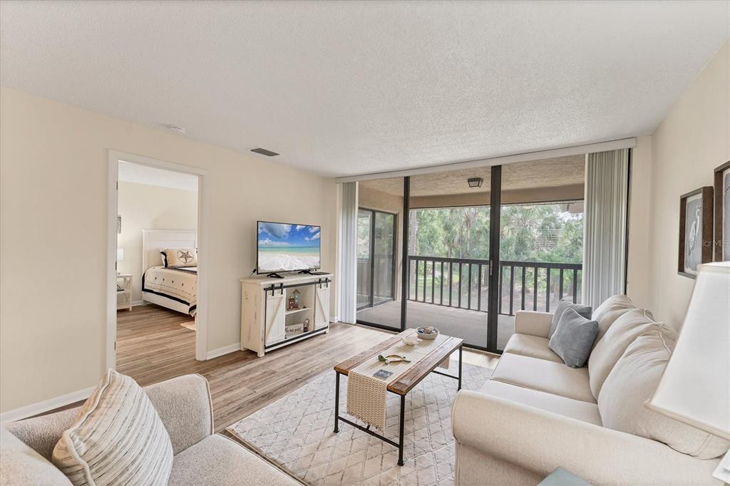 A living room with light-colored furniture, a television, wood-look flooring, and a sliding glass door — 5264 LAKE VILLAGE DRIVE UNIT 48, SARASOTA, FL