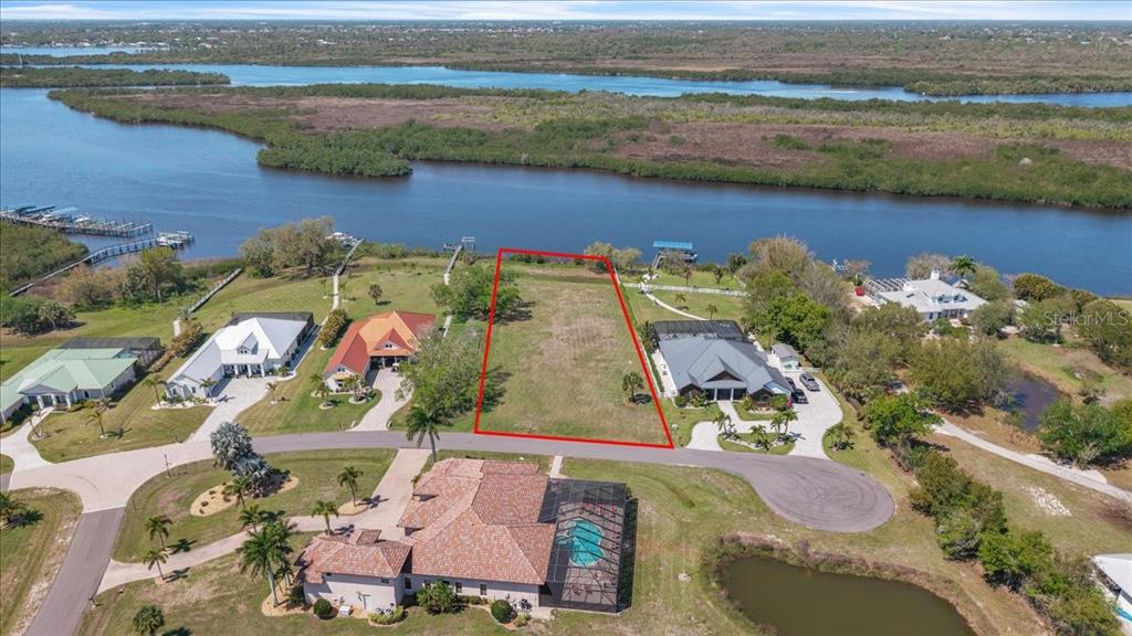 An aerial view shows a vacant waterfront lot outlined in red between two residential homes — 2009 TREASURE LANE, PUNTA GORDA, FL