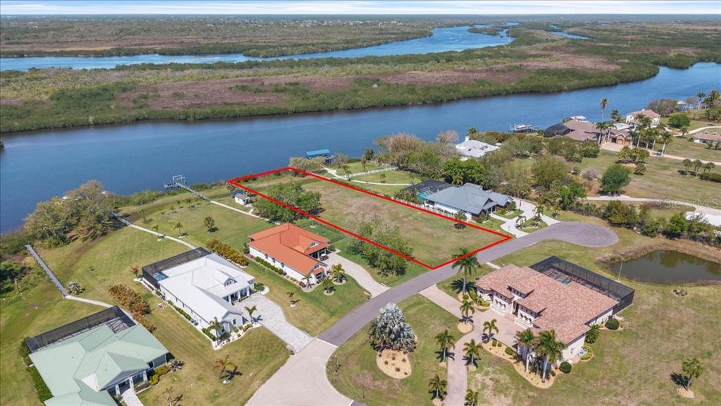 An aerial view shows a vacant rectangular waterfront lot outlined in red between two houses — 2009 TREASURE LANE, PUNTA GORDA, FL