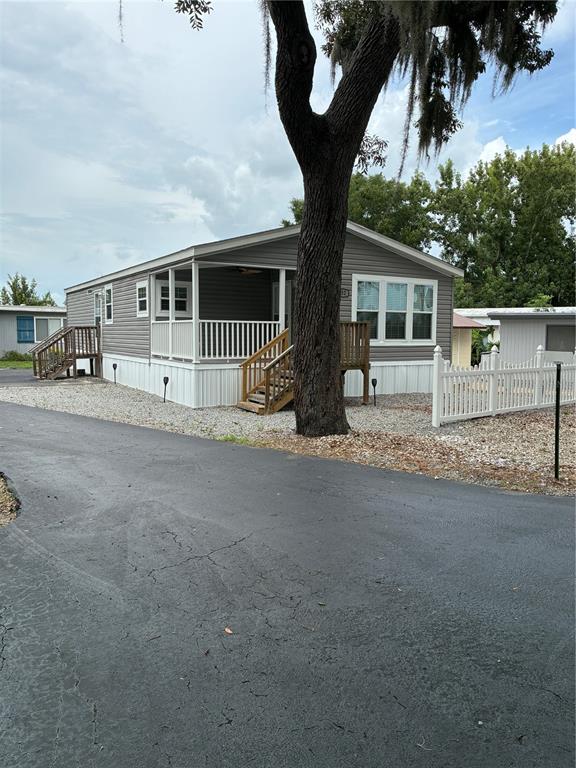 A gray manufactured home features a front porch, a large tree, and a white fence — 3896 PICCIOLA ROAD UNIT 532, FRUITLAND PARK, FL
