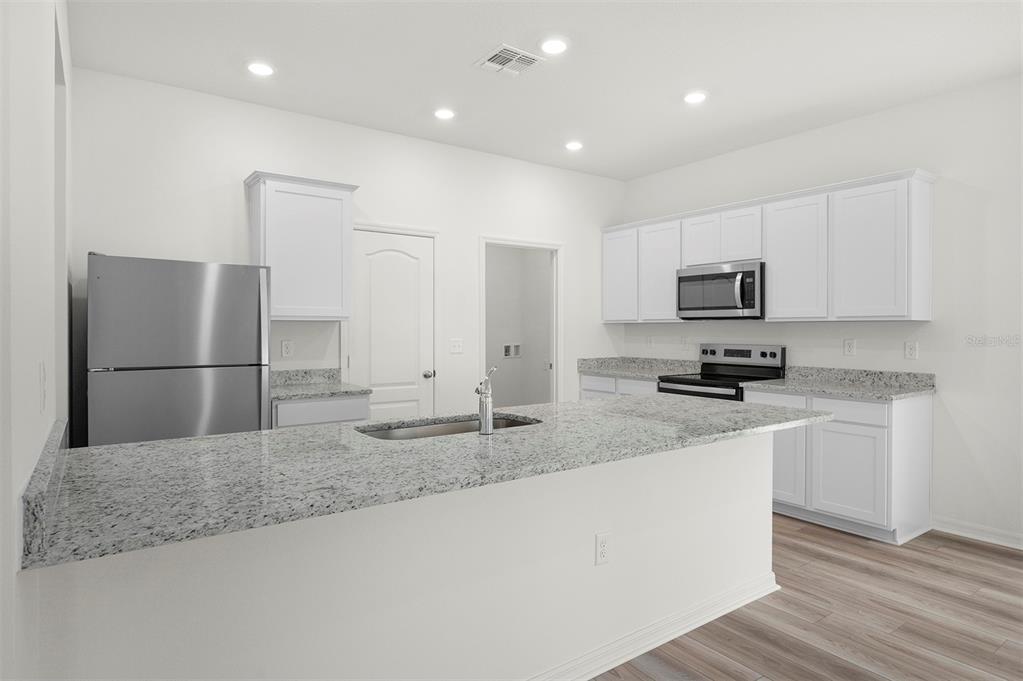 A kitchen with white cabinets, granite countertops, stainless steel appliances, and a breakfast bar — 13347 TULA LOOP, ASTATULA, FL