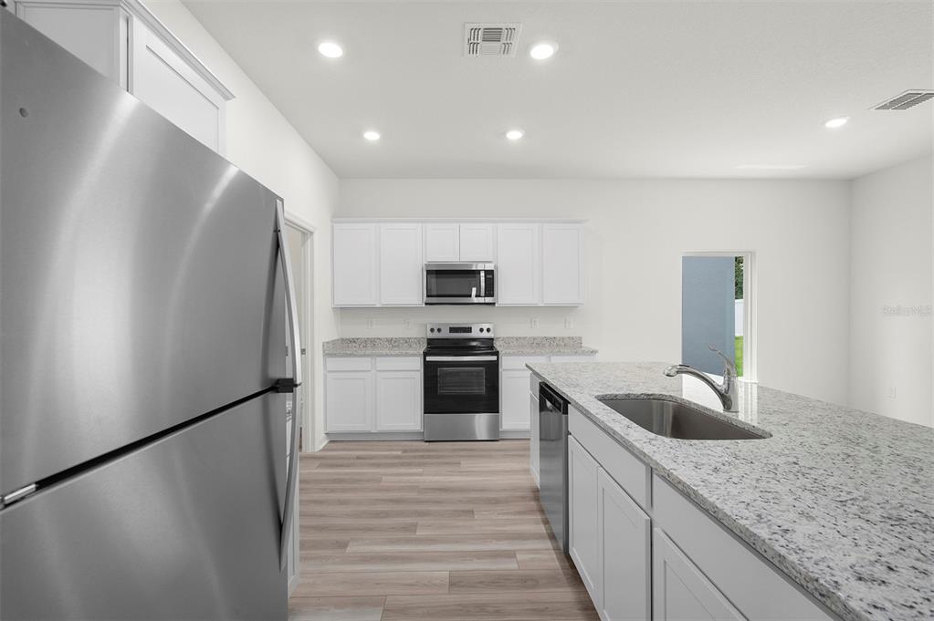 A modern kitchen features white cabinets, granite countertops, stainless steel appliances, and light wood flooring — 13347 TULA LOOP, ASTATULA, FL