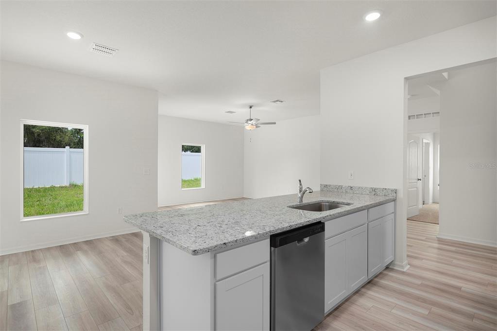 A kitchen island with a granite countertop and stainless steel dishwasher overlooks an open living area — 13347 TULA LOOP, ASTATULA, FL