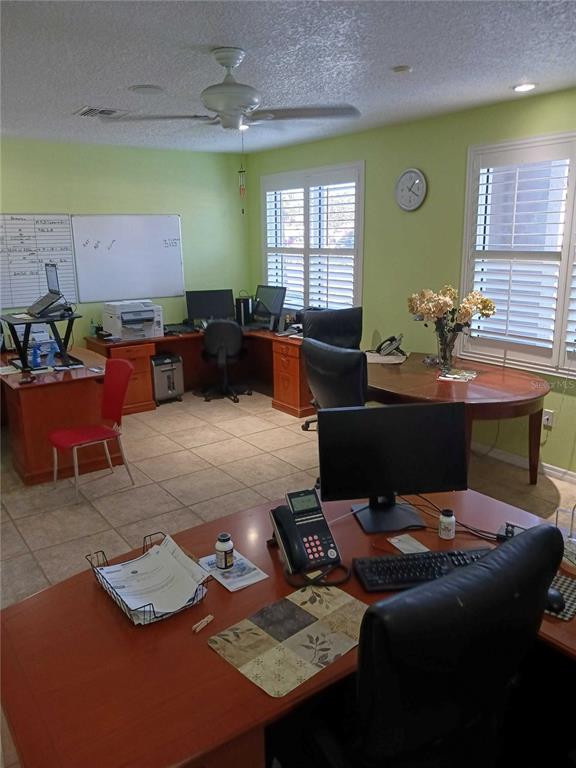 A home office features multiple wooden desks, computer equipment, a whiteboard, and tile flooring — 515 27TH STREET E UNIT 7, BRADENTON, FL