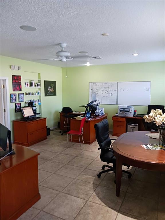 An office space features light green walls, tile flooring, wooden desks, and a white ceiling fan — 515 27TH STREET E UNIT 7, BRADENTON, FL
