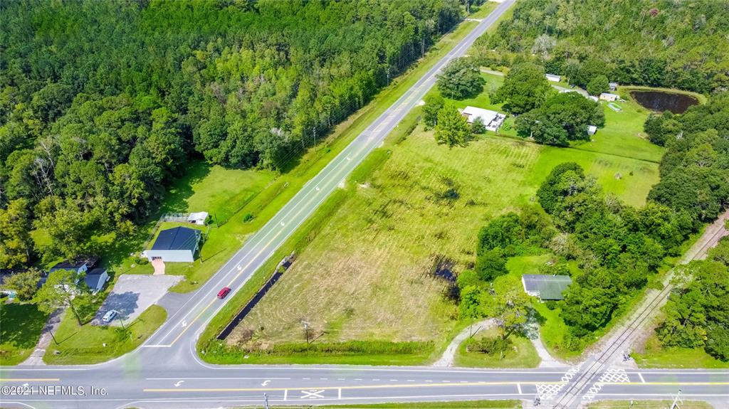 An aerial view shows a large, grassy lot situated between a road and a forest — 10422 SE SR 100, STARKE, FL