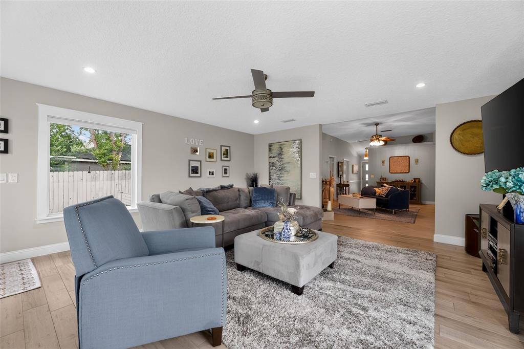 A living room features a grey sectional, a blue armchair, and light wood-look flooring — 590 ASHCROFT LANDING DRIVE, JACKSONVILLE, FL