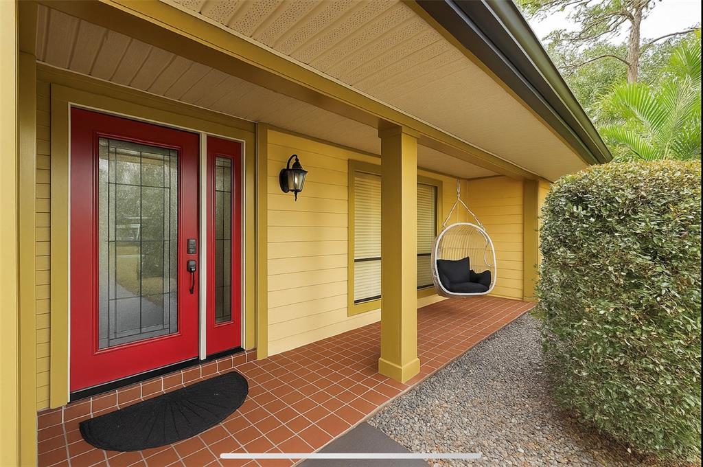 A covered porch with yellow siding, a red front door, and a hanging egg chair — 414 TIMBERCOVE CIRCLE, LONGWOOD, FL