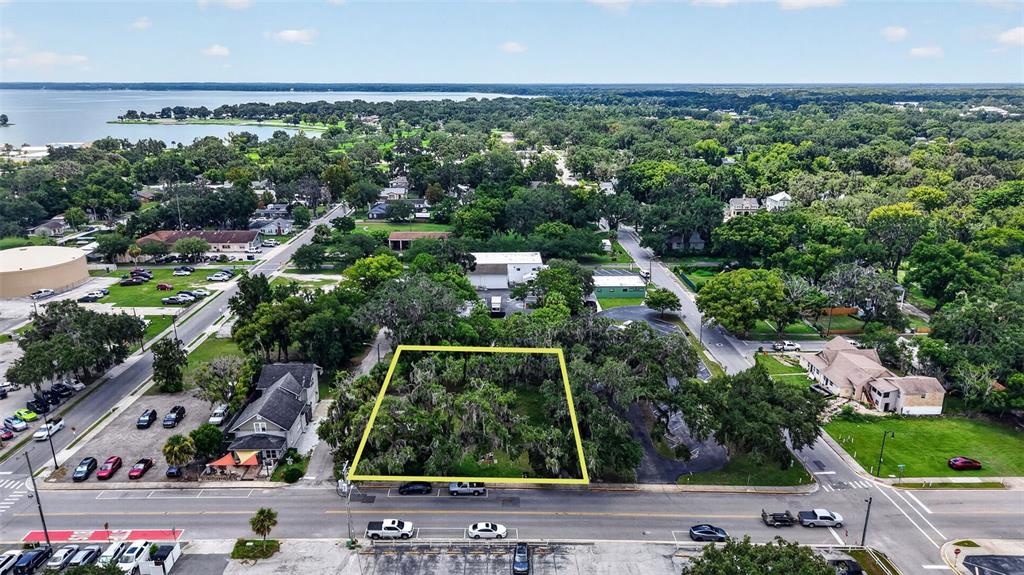 An aerial view shows a vacant, tree-covered lot outlined in yellow near a paved road — 703 W MAGNOLIA STREET, LEESBURG, FL