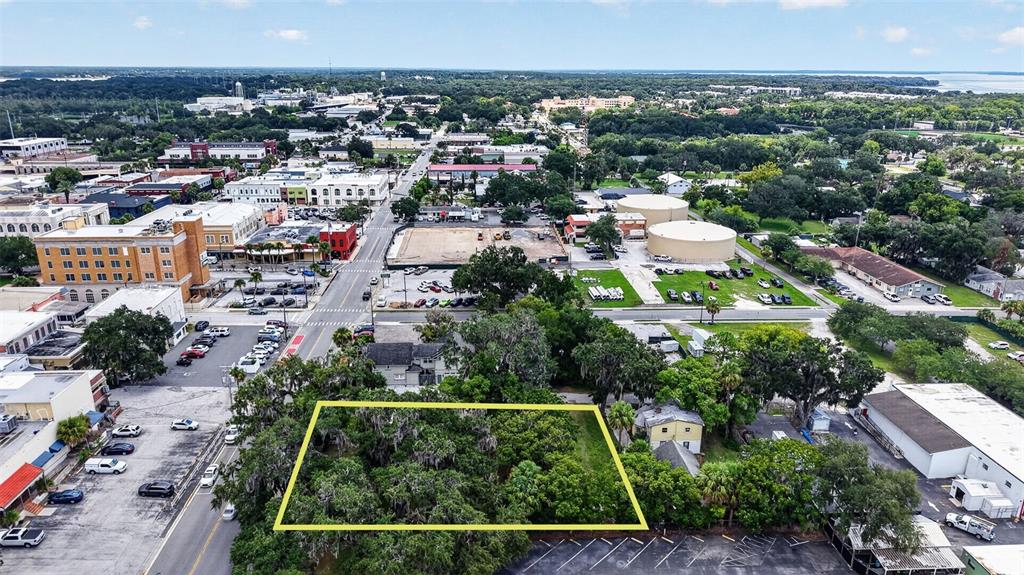 An aerial view shows a wooded lot outlined in yellow near a city street — 703 W MAGNOLIA STREET, LEESBURG, FL