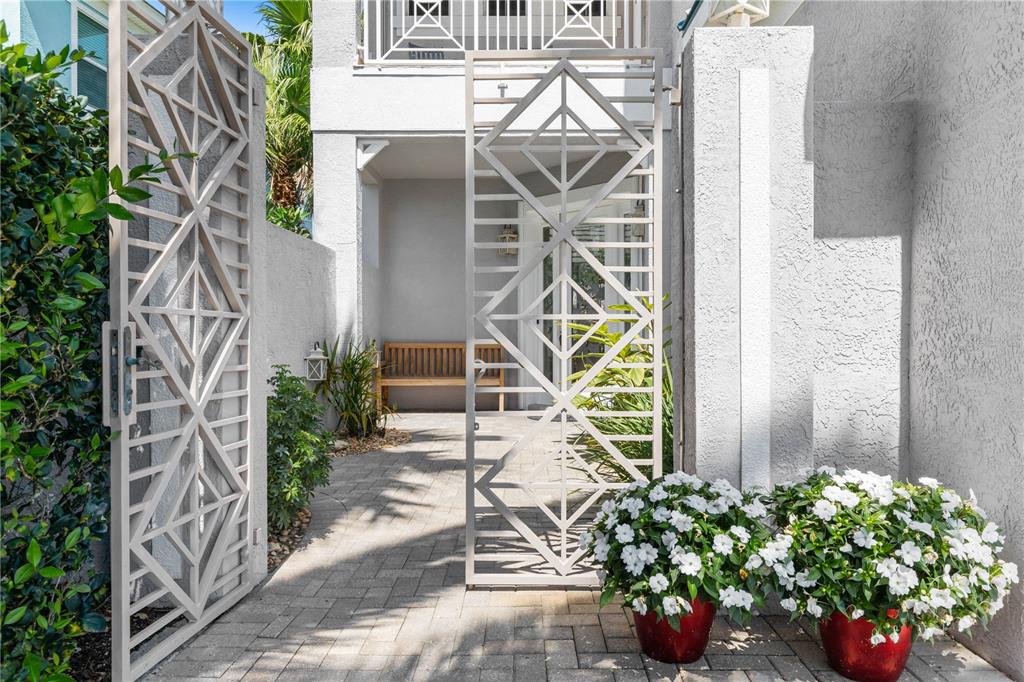 A paved entryway features decorative metal gates, potted white flowers, and a wooden bench — 12 CINNAMON BEACH WAY, PALM COAST, FL