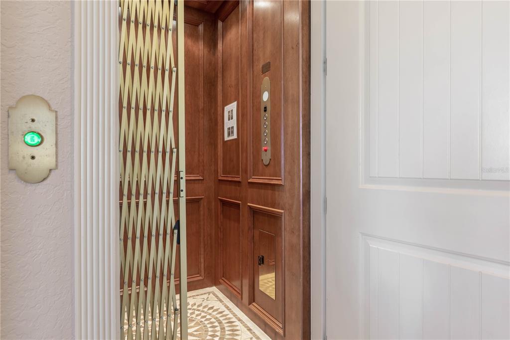 An elevator with wood paneling and a gold accordion gate sits beside a white door — 12 CINNAMON BEACH WAY, PALM COAST, FL