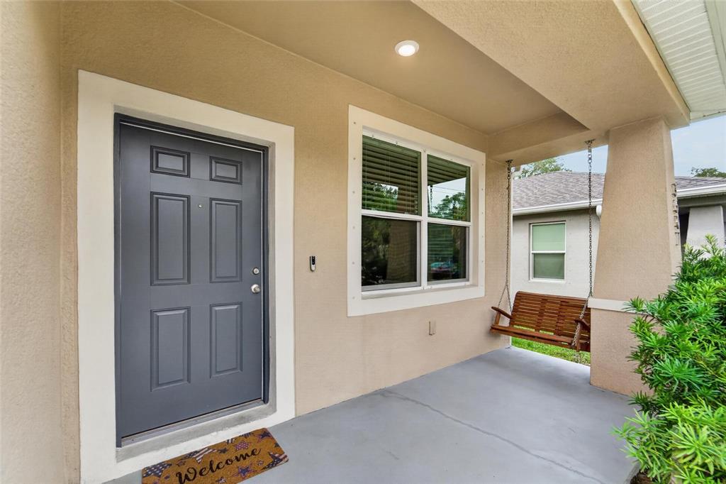 A covered front porch features a gray door, a window, and a wooden hanging swing — 3507 E 10TH AVENUE, TAMPA, FL