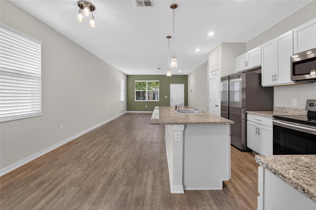 An open-concept kitchen and living area featuring white cabinets, granite countertops, and wood-look flooring — 3507 E 10TH AVENUE, TAMPA, FL