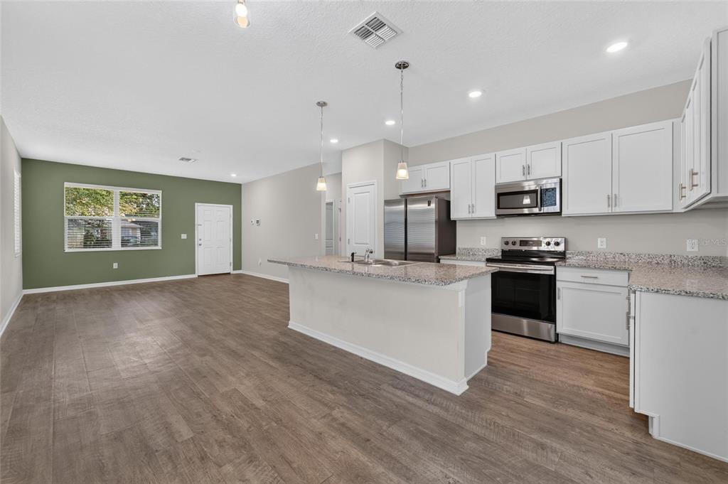 An open-concept kitchen and living area with white cabinets, granite countertops, and wood-look flooring — 3507 E 10TH AVENUE, TAMPA, FL